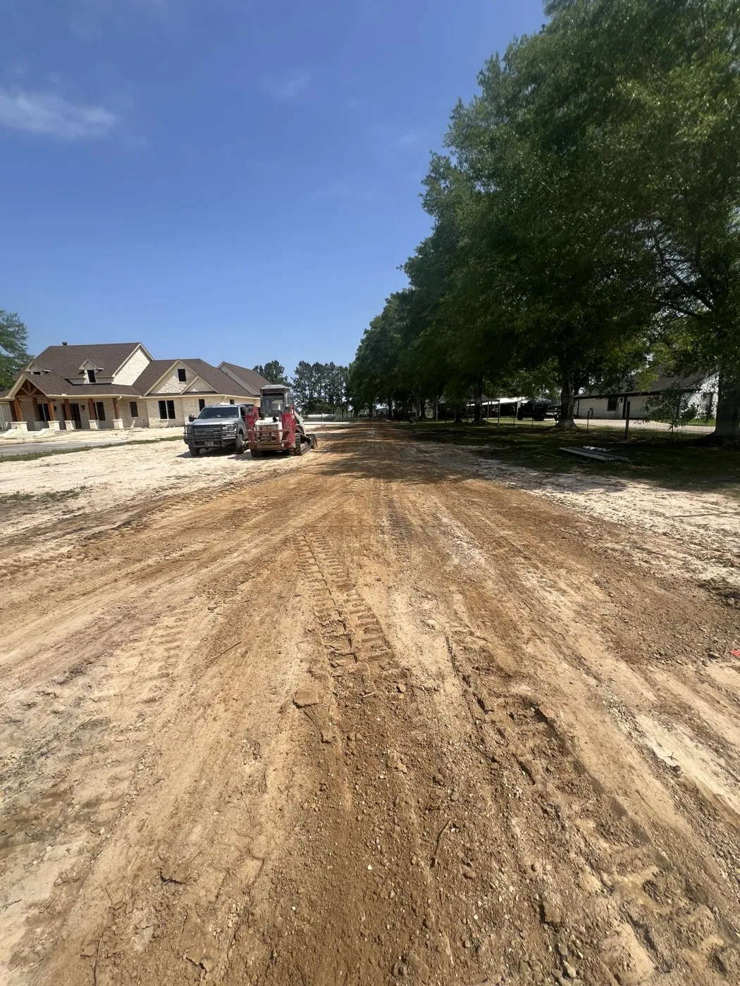 Wide dirt drive graded with equipment working near new homes