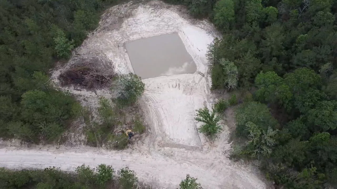 Finished pond holding water with shaped sandy banks in the pines